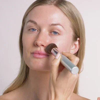 Women applying powder foundation on her face using brush