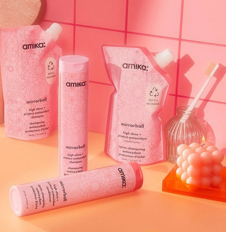 Amika Mirrorball shampoo and conditioner in pink packaging, with decorative soap and a toothbrush.
