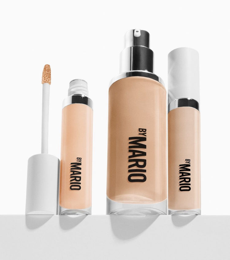 Four makeup products from makeup by mario in sleek packaging: a foundation, concealer, and two applicators.