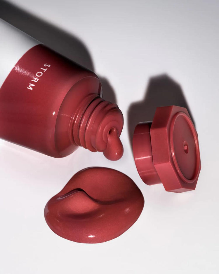 Glossier Cloud Paint in "Storm" shown with product squeezed out. The tube lies horizontal next to the cap, with a dollop of the "Storm" shade.