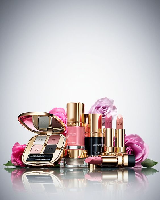 A collection of luxurious D&G cosmetics, including lipsticks, foundation, and eyeshadow, elegantly arranged with pink roses.