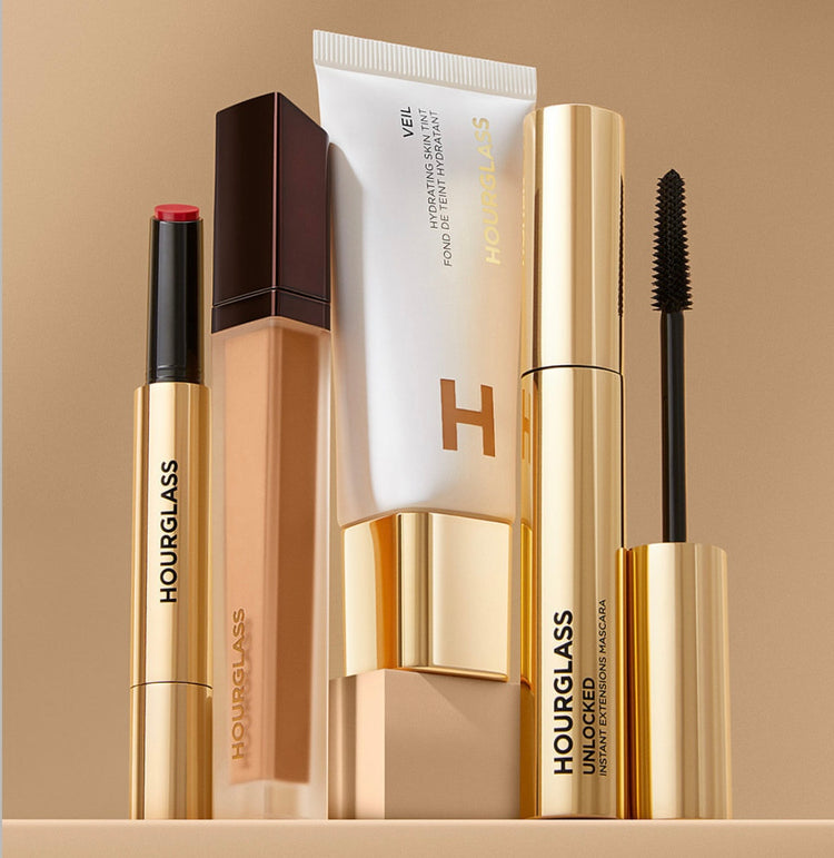 Collection of Hourglass makeup products: a red lip stick, foundation, hydrating veil, and mascara.