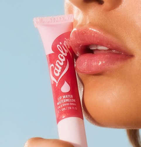 Close-up of a woman's lips coated in glossy lip gloss, holding a tube of Lanolips Watermelon Lip Water.