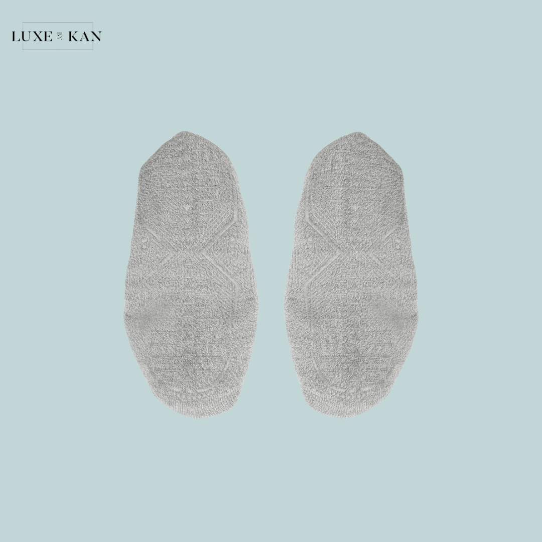 A pair of soft, light grey socks laid flat on a soft blue background, featuring textured patterns for style and comfort.