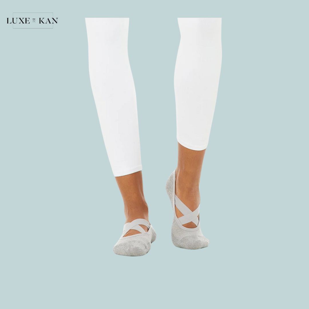 A pair of legs in white leggings, wearing light grey ballet flats with criss-cross straps.