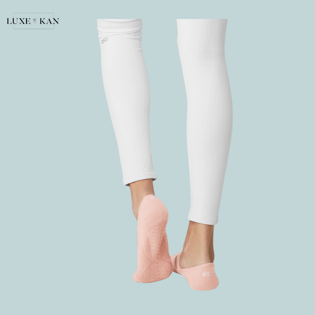 Feet wearing pink backless socks, styled with white leggings, against a soft blue background. Elegant and casual look for activewear.