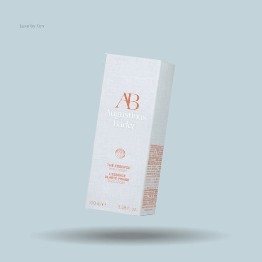 Augustinus Bader "The Essence" product box with minimalist white design against light blue backdrop.