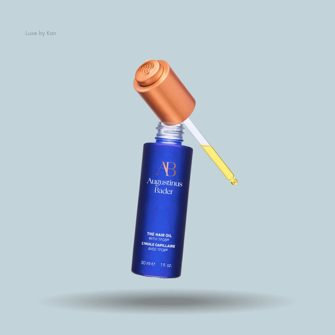 A blue bottle of Augustinus Bader Hair Oil with TFC8, featuring a gold cap and dropper.