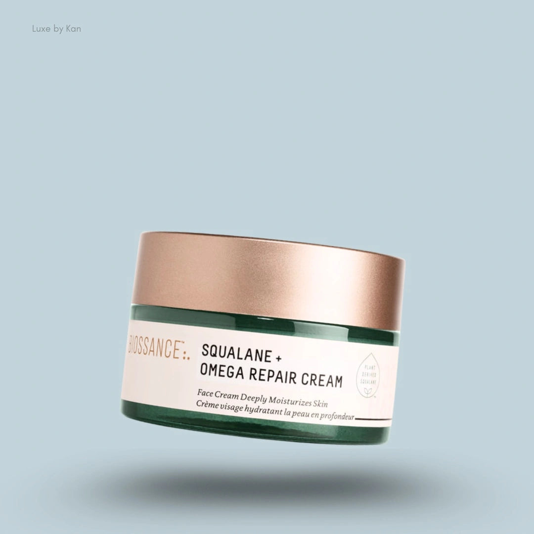Biossance squalane + omega repair cream in a green container with brown lid on a blue background.