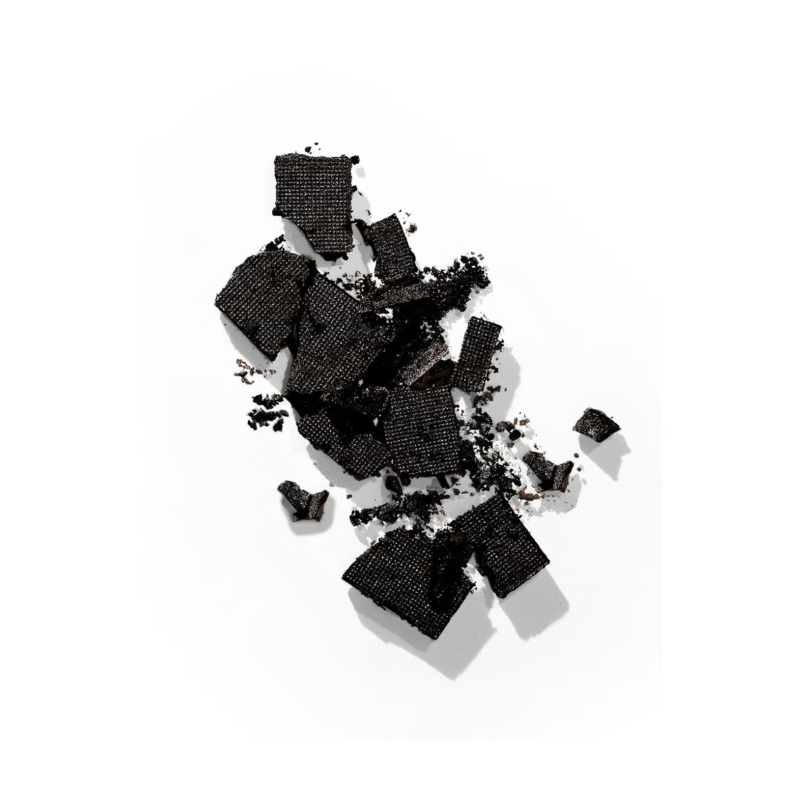 Color Wow Root Cover Up with fragments of textured black material scattered on a white surface, highlighting a mix of larger pieces and fine particles.