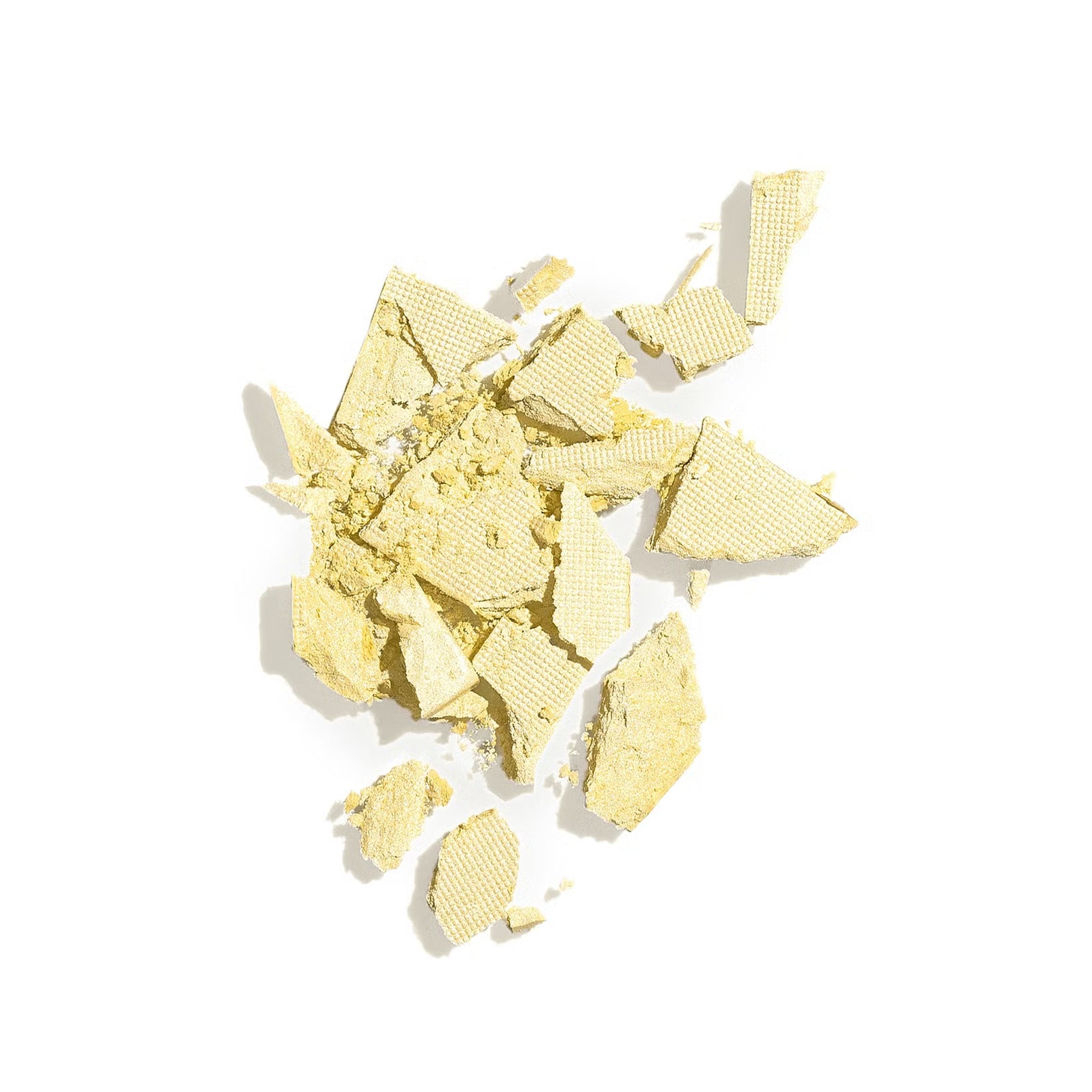 Color Wow Root Cover Up with crushed yellow makeup powder scattered across a white surface, featuring angular fragments and fine dust particles.