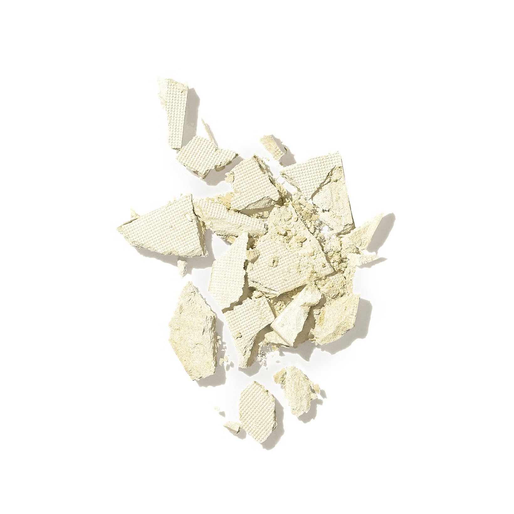 A scattered pile of broken, pale yellow textured fragments against a white background, resembling crushed dry material.
