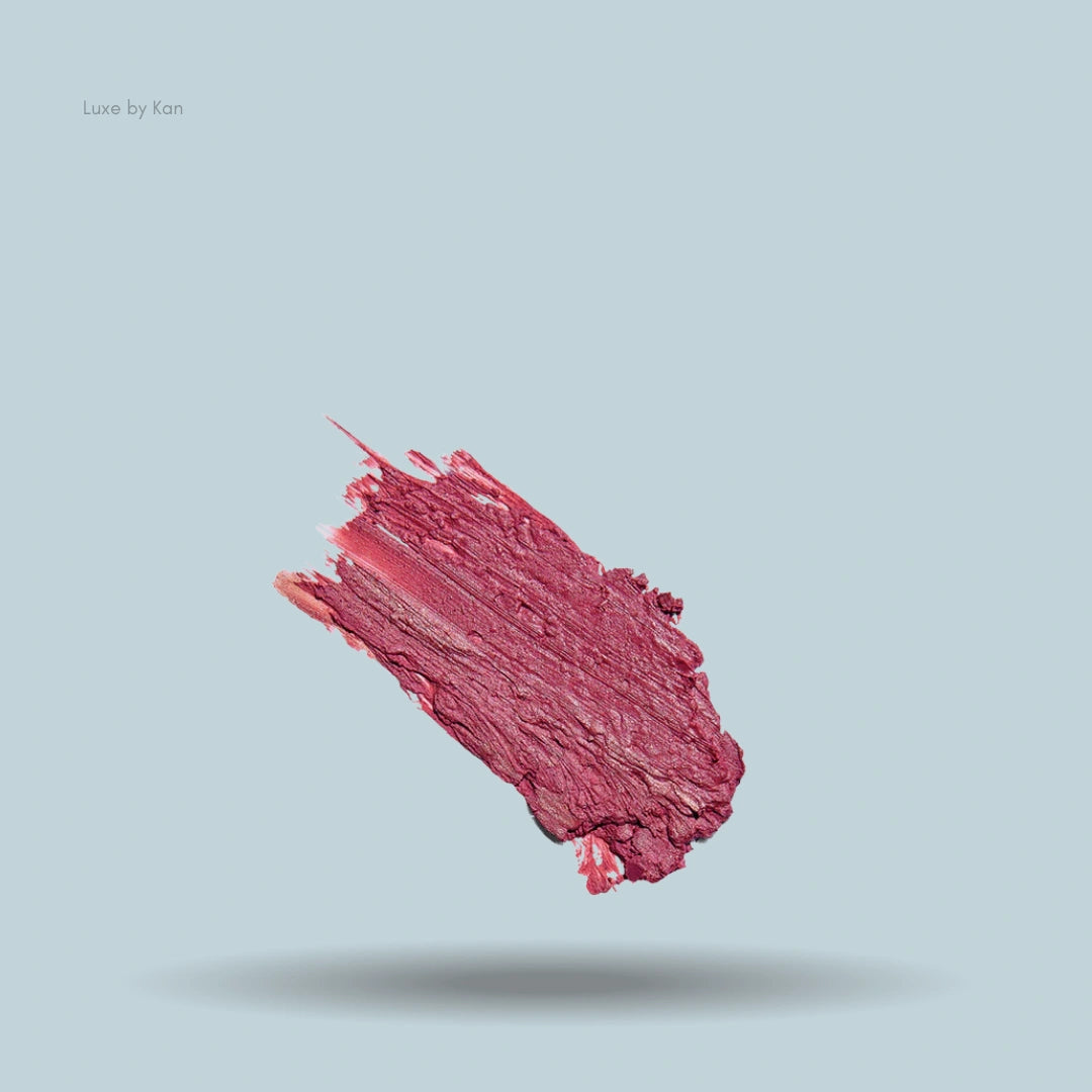 Close-up of a pinkish-red smear of Colorescience Sunforgettable Total Protection Color Balm SPF 50 on a powder-blue background, casting a shadow below.
