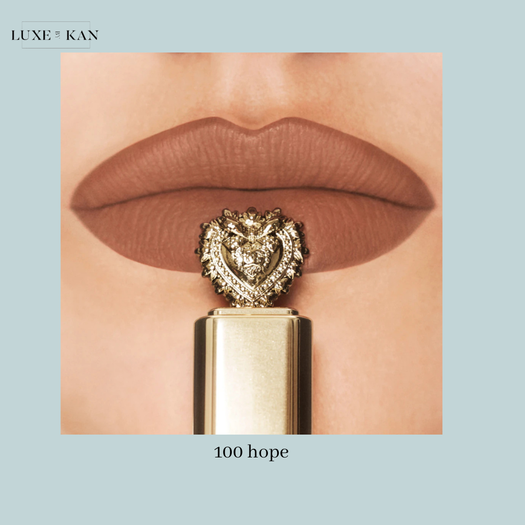 Close-up of matte brown lips holding a gold lipstick tube topped with a heart-shaped embellishment, labeled "100 hope."