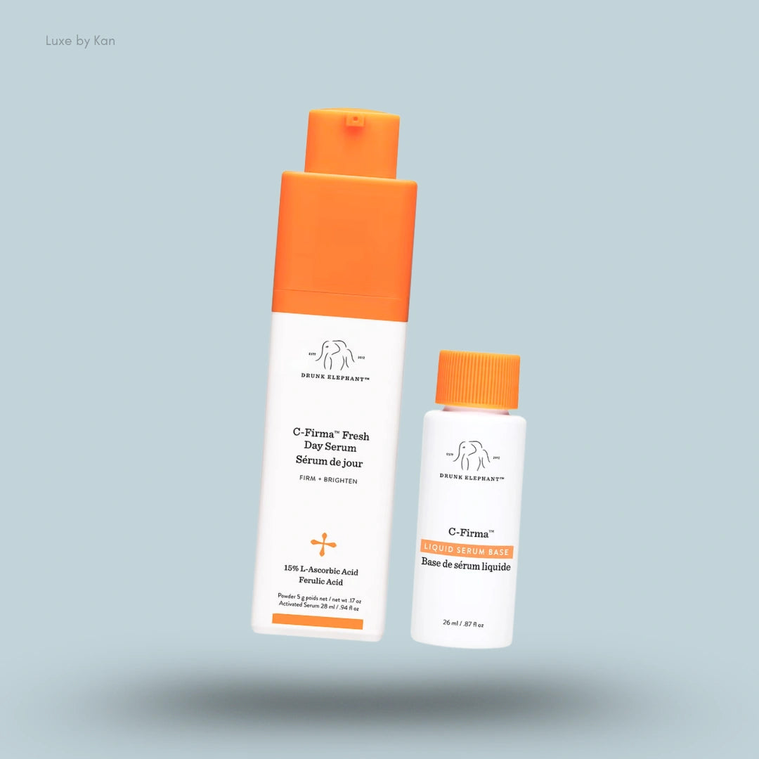 Drunk Elephant C-Firma Fresh Day Serum and Liquid Serum Base products with orange caps against a light blue background.