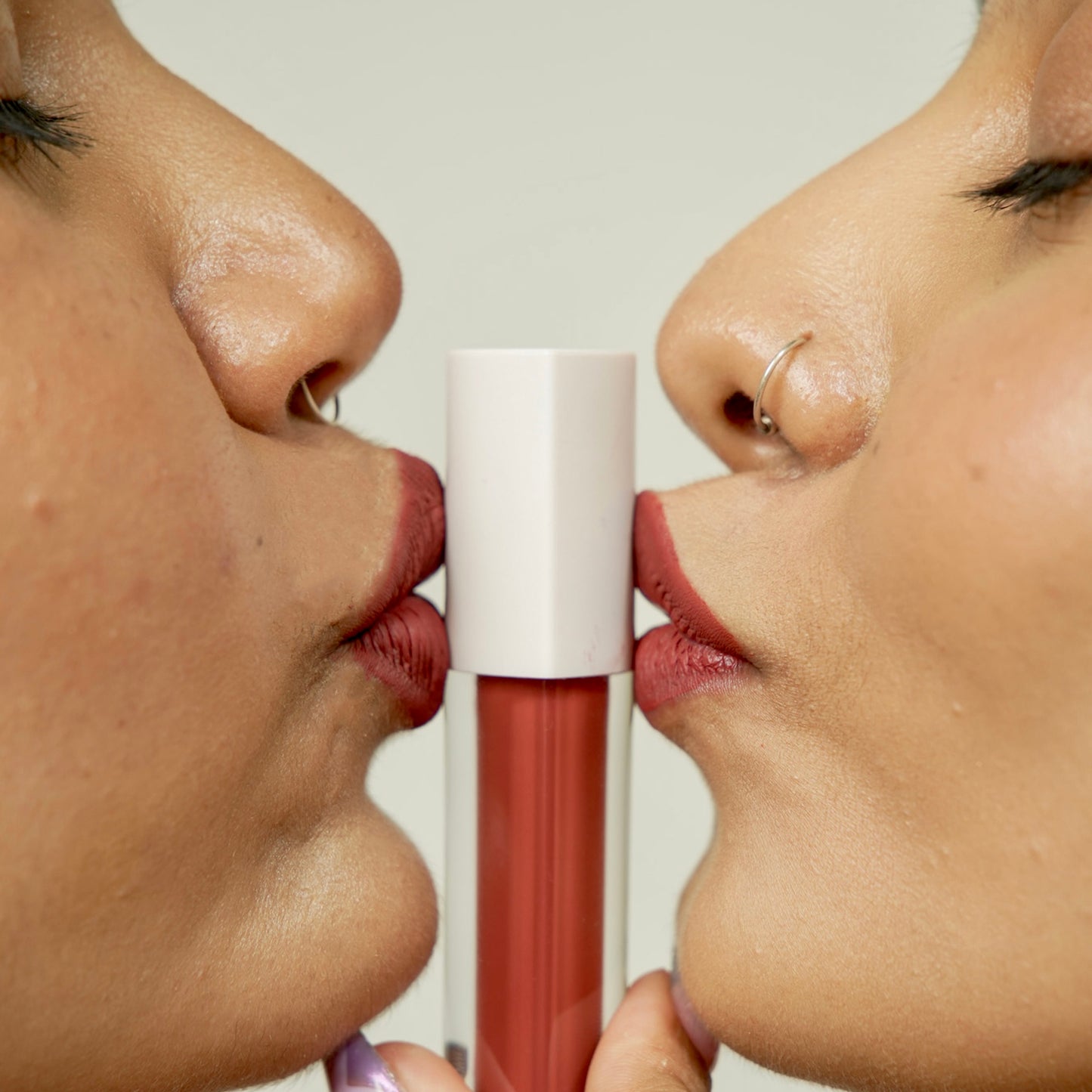 A close-up of lips applying a liquid lipstick, showcasing a rich, matte red shade and a sleek white tube.