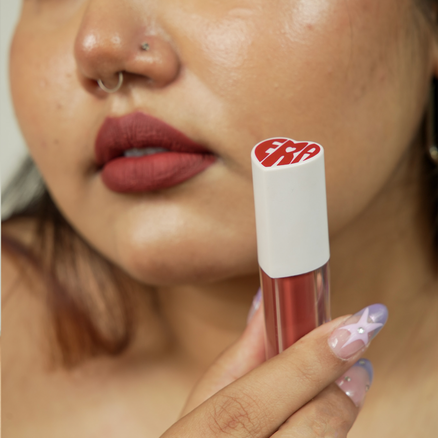 A close-up of a hand holding a era beauty rom-com lipstick shade product.