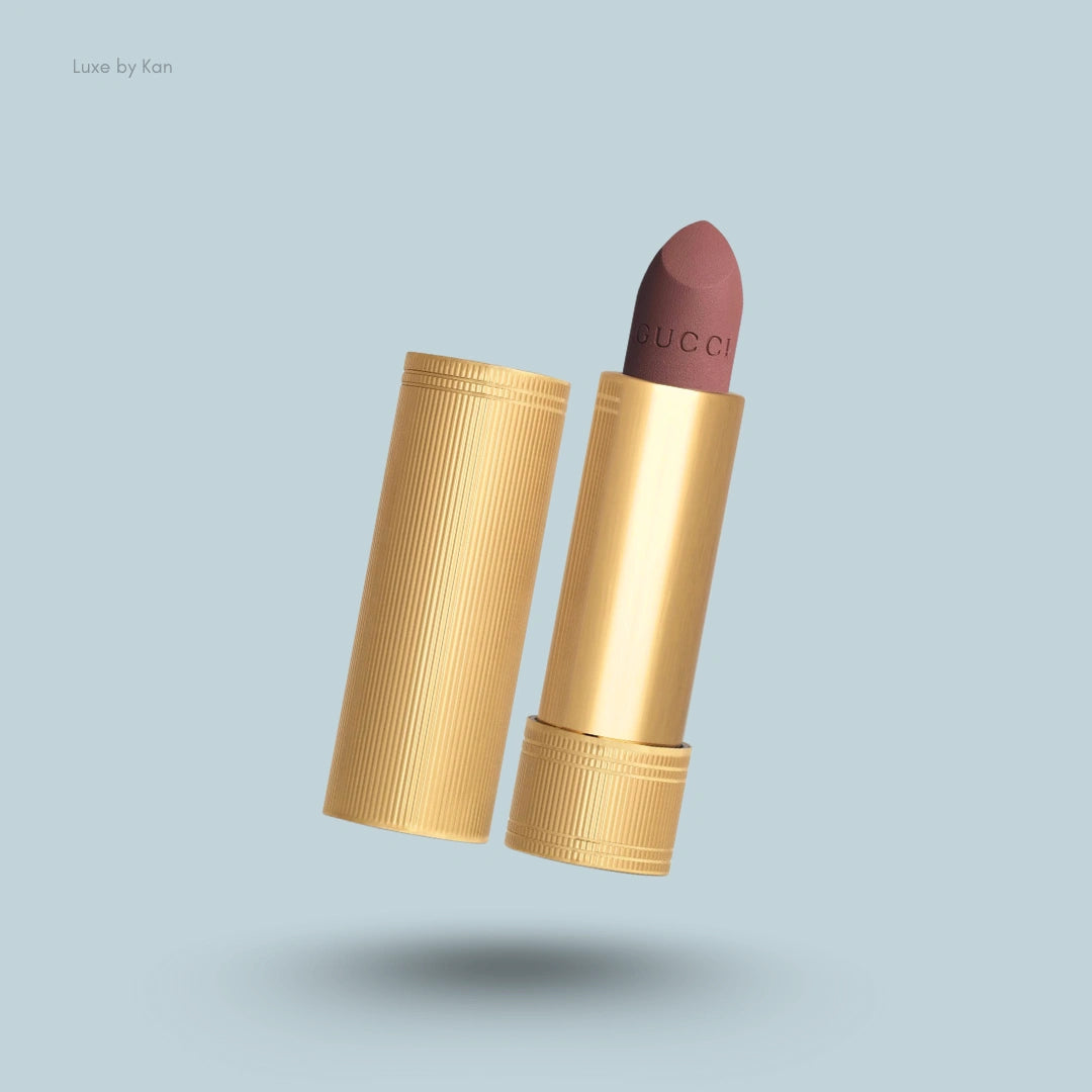 Open Gucci Rouge à Lèvres Matte lipstick with a ribbed gold tube and mauve color against a pale blue background.