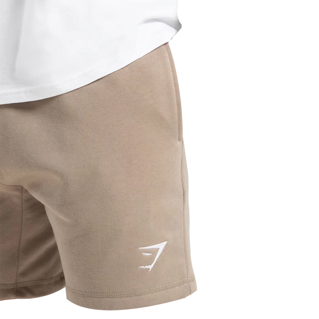 Close-up of a pair of khaki Gymshark men's Crest shorts, featuring a slim fit and the Gymshark logo.