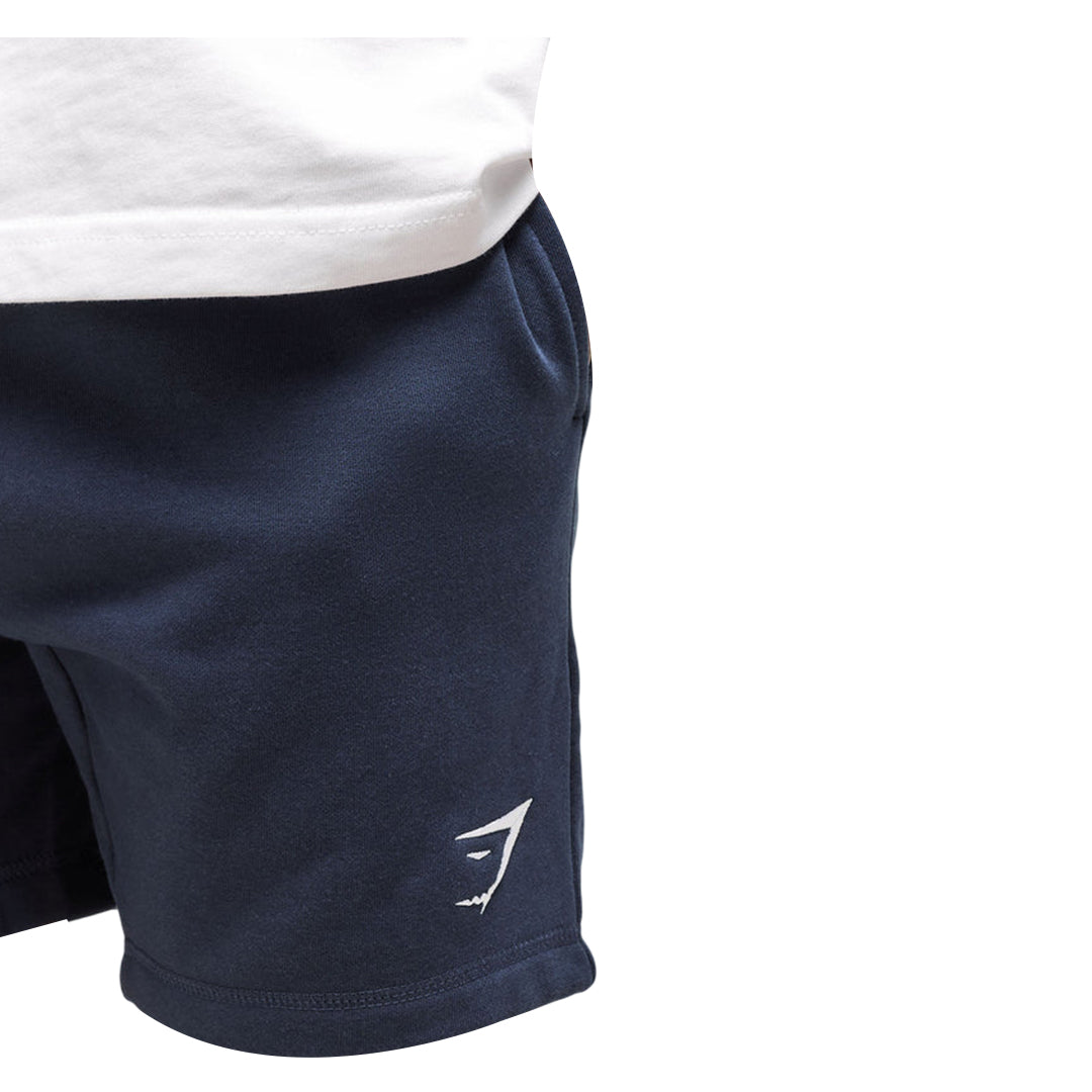 Close-up of navy blue Gymshark men's crest shorts with a white logo on the lower right leg and a partial view of a white shirt.