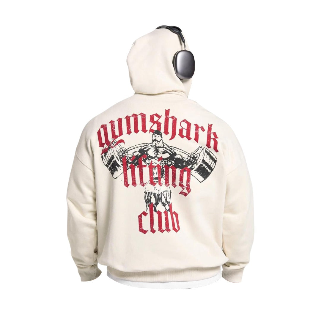 A person wearing a cream hoodie featuring a vintage-style graphic of a muscular figure lifting weights, with "Gymshark Lifting Club" text.