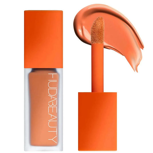 A Huda Beauty faux filter color corrector in an orange tube, alongside a doe-foot applicator and a swatch of orange product.