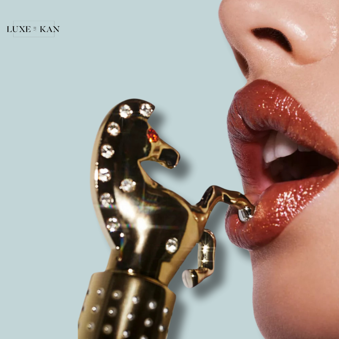 Close-up of a woman’s lips applying lipstick with a glamorous gold horse-shaped applicator adorned with rhinestones.