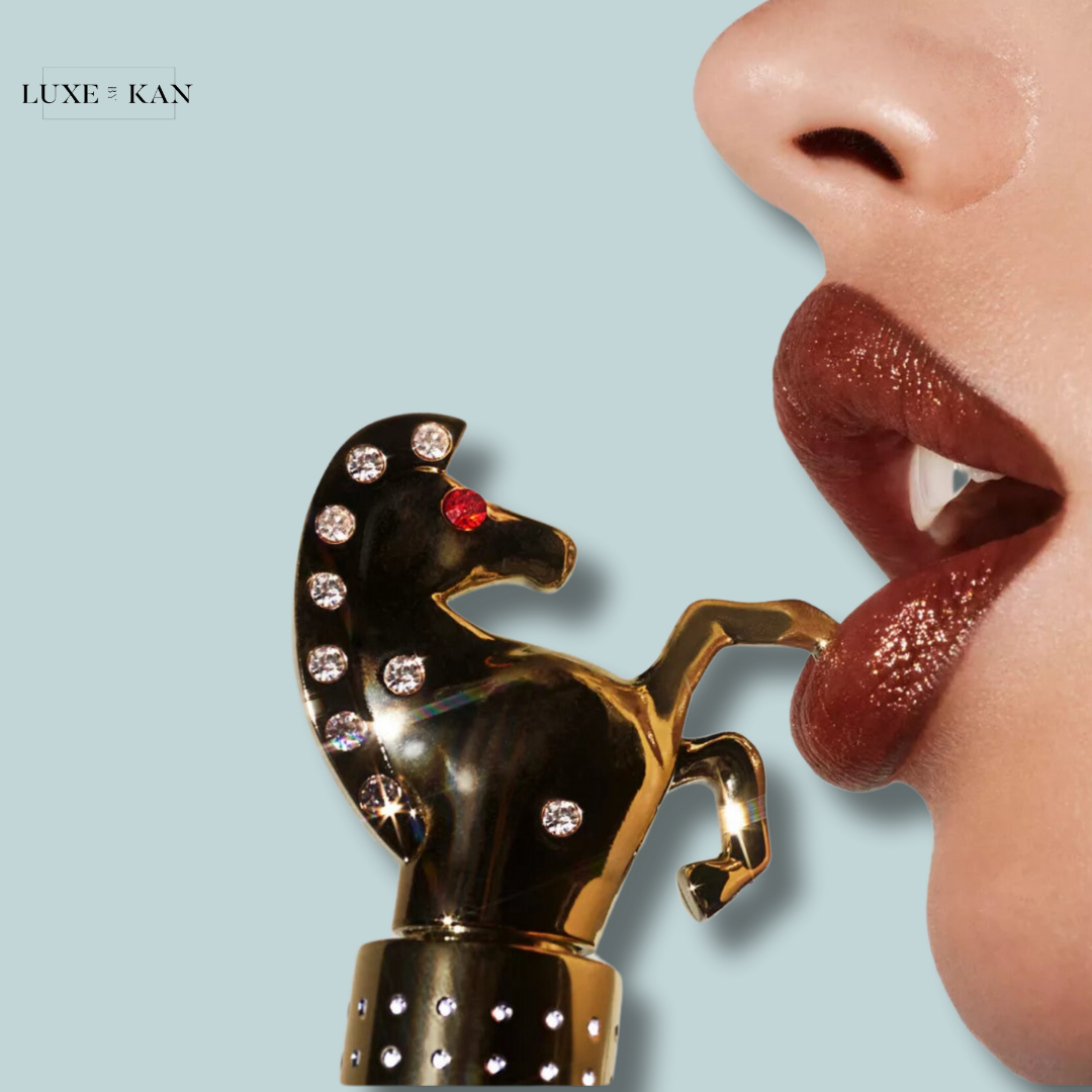 Close-up of a woman's lips with glossy brown lipstick, holding a jeweled horse-shaped lipstick case against her mouth.