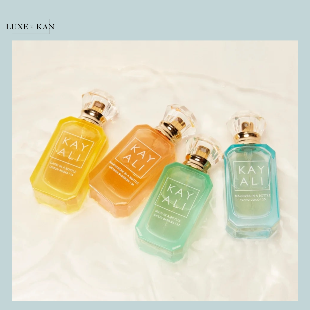 Four colorful KAYALI perfume bottles—yellow, orange, green, and blue—arranged stylishly on a soft, white surface.