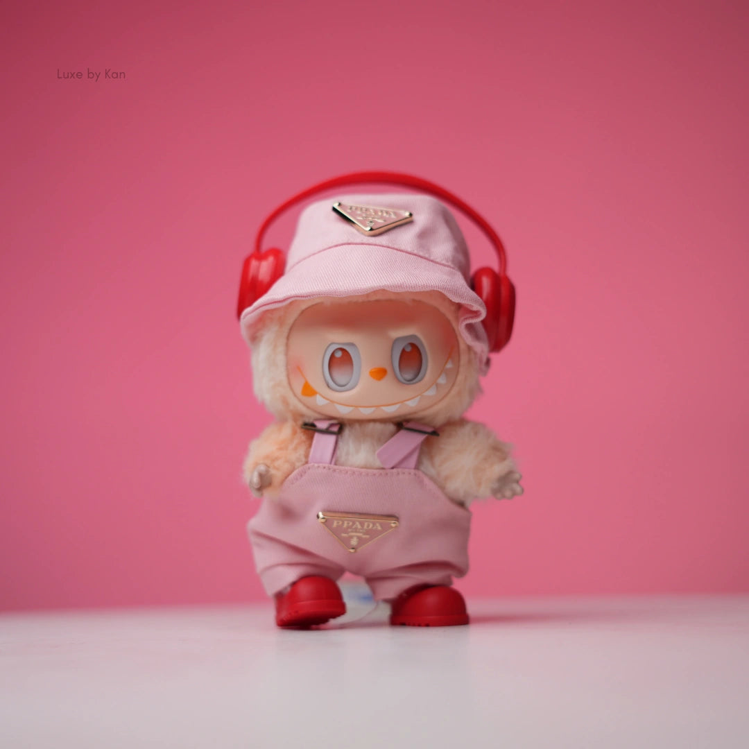 Labubu doll wearing a light pink Prada-branded bucket hat, matching overalls, red shoes, and red headphones.