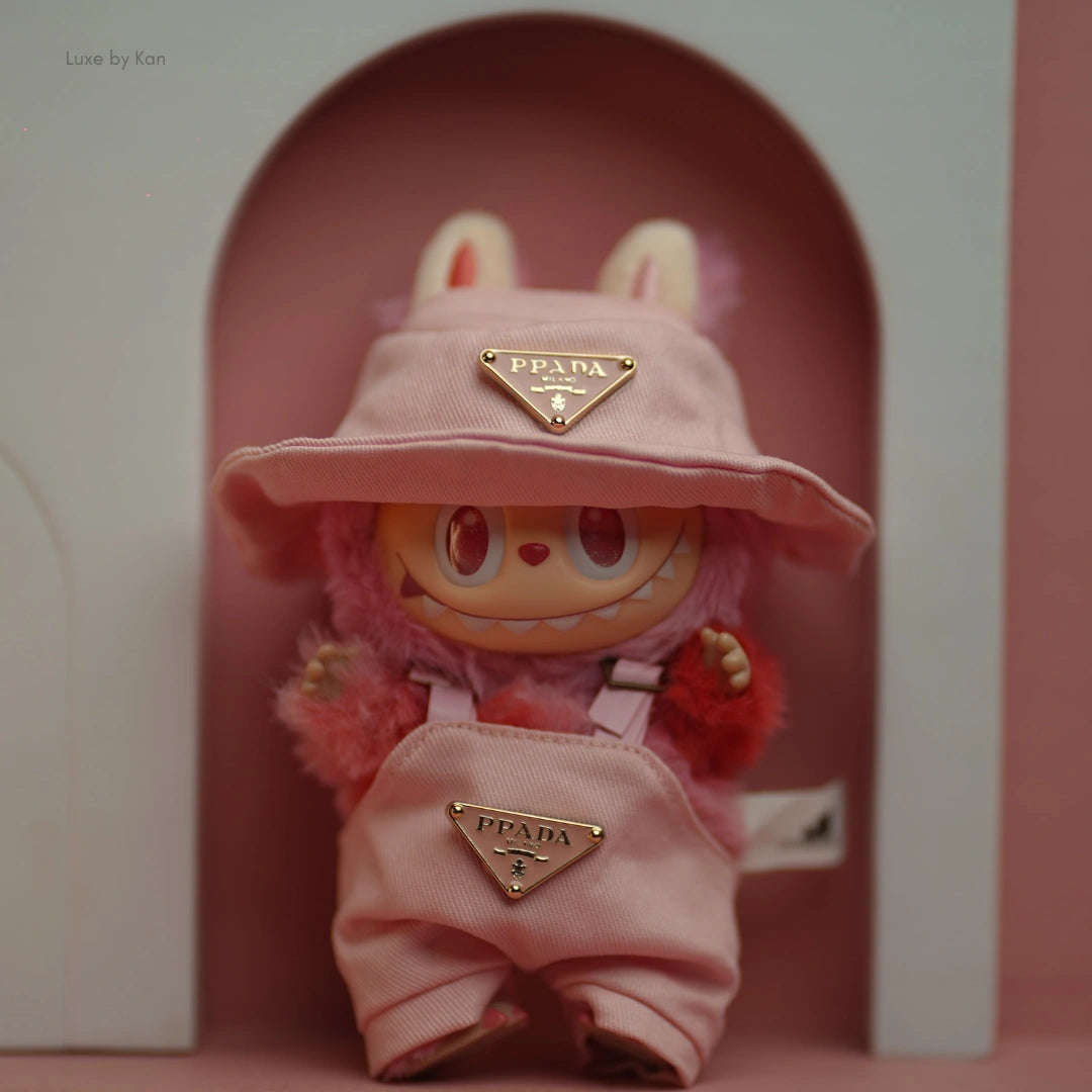 Close-up of Labubu Pink Luxe toy figure wearing pink overalls and a matching bucket hat, both adorned with Prada logos.