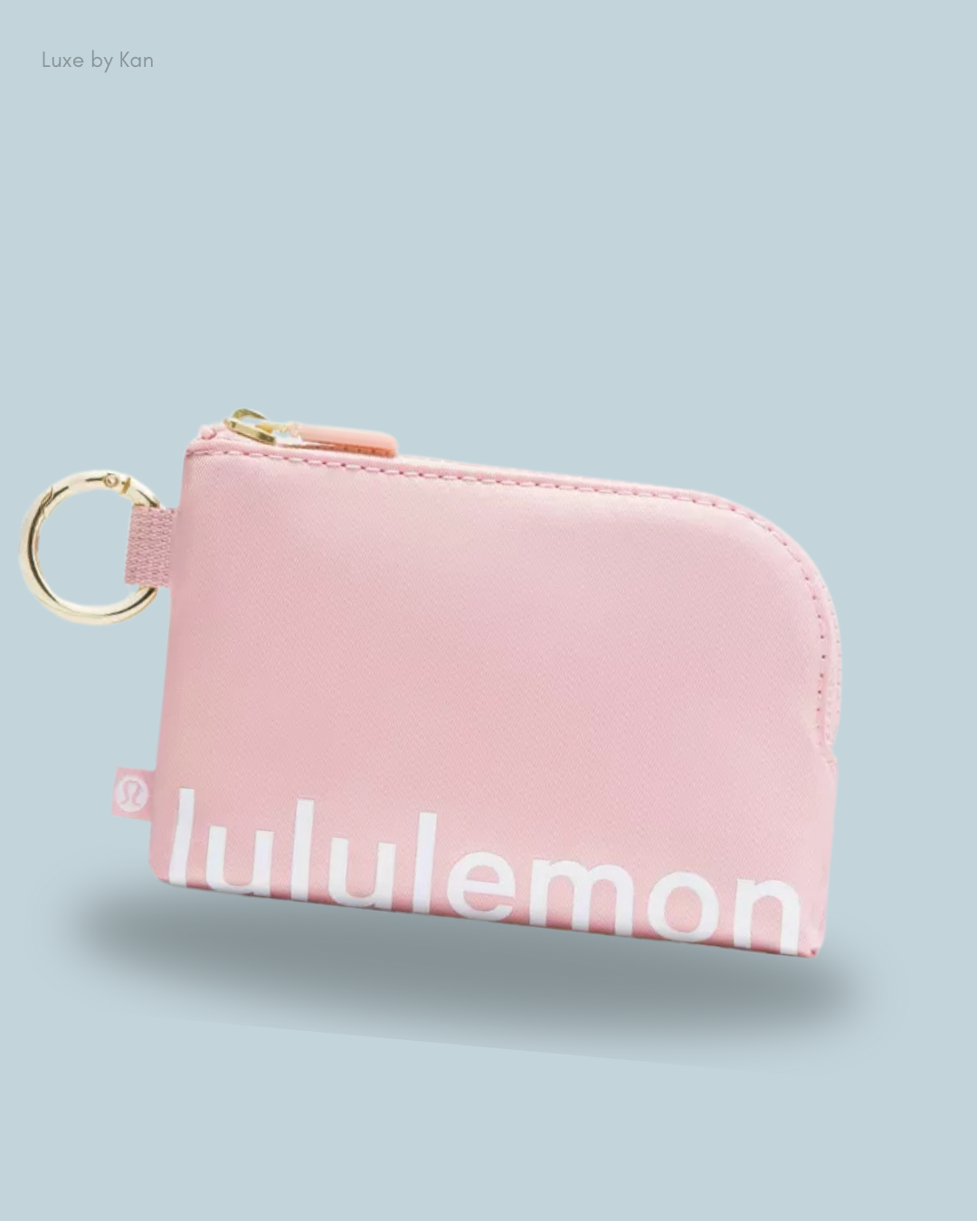 A smooth pink Lululemon pouch with a gold zipper and keyring, resting on a light blue background.