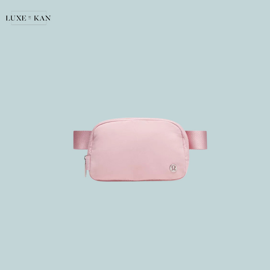A soft pink waist pouch with a sleek design and a logo, set against a light blue background. Ideal for stylish storage on the go.