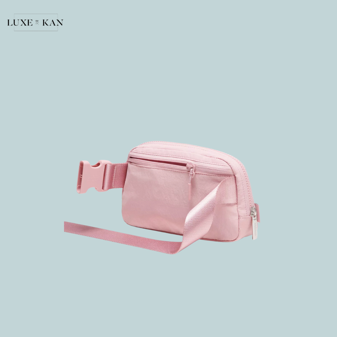 Light pink crossbody bag with a front zipper and a smooth strap, set against a soft blue background. Simple and stylish accessory.