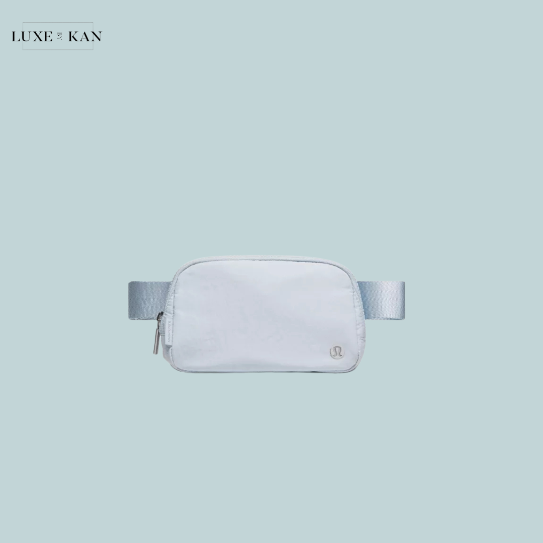 A sleek white fanny pack with a light blue strap, featuring a minimalist design and a small logo.