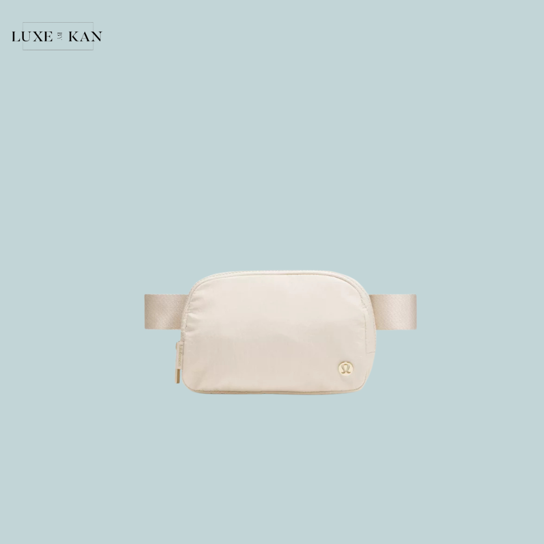 A sleek, cream-colored fanny pack with a minimalist design and a logo.
