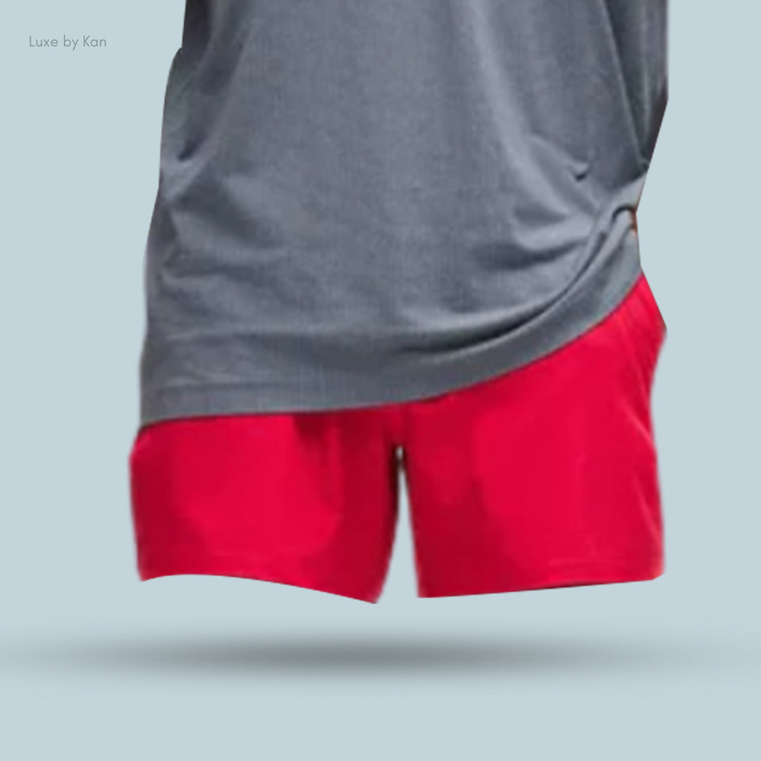 A close-up of a model’s torso wearing a gray athletic shirt and vibrant red shorts against a light blue background.