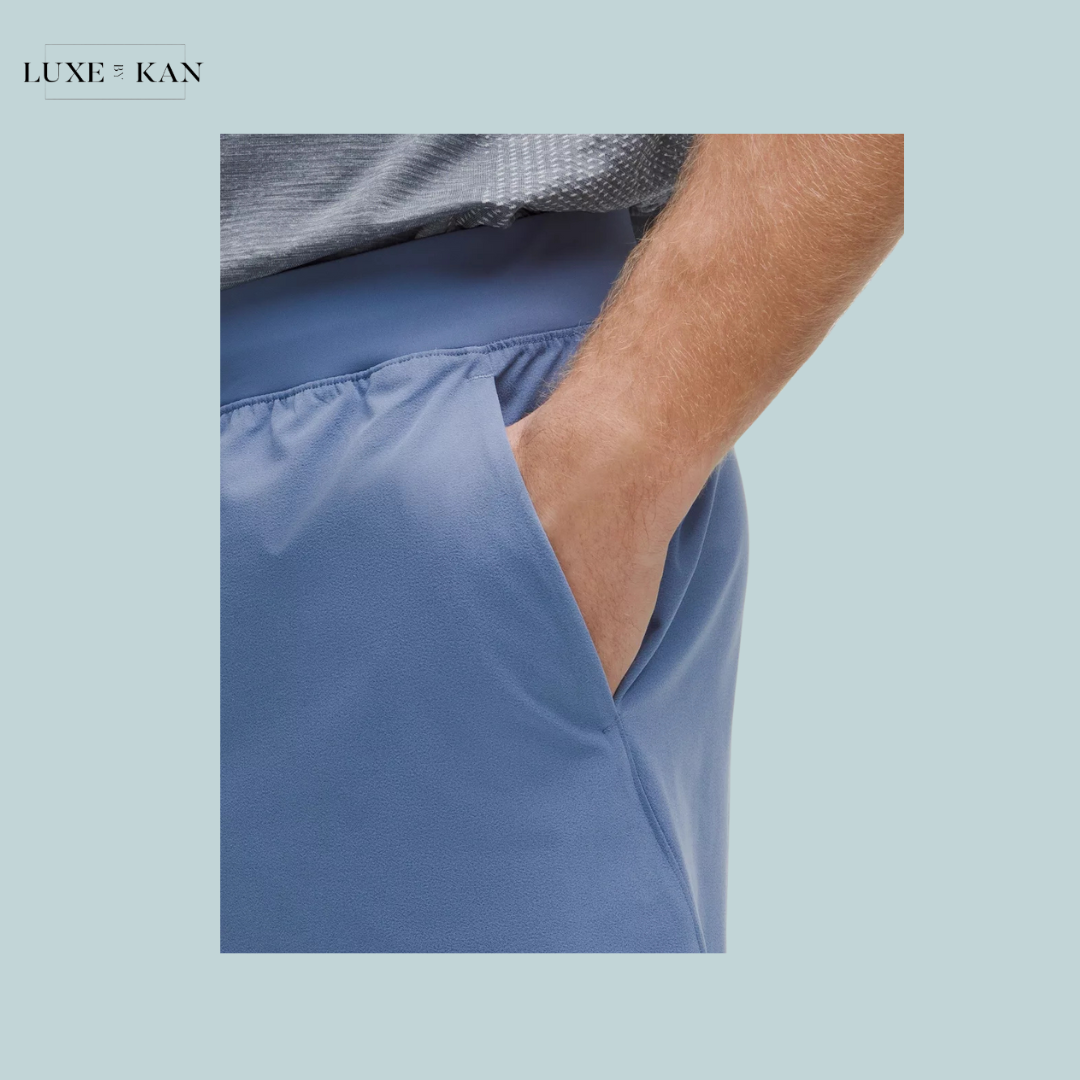 A close-up of a man's hand in the pocket of stylish blue shorts, with a gray sporty shirt.