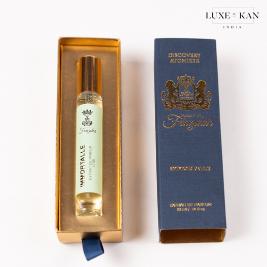 A luxurious fragrance bottle labeled "Immortalle" inside a gold box next to an elegant navy blue packaging from Maison de Fauzdar.