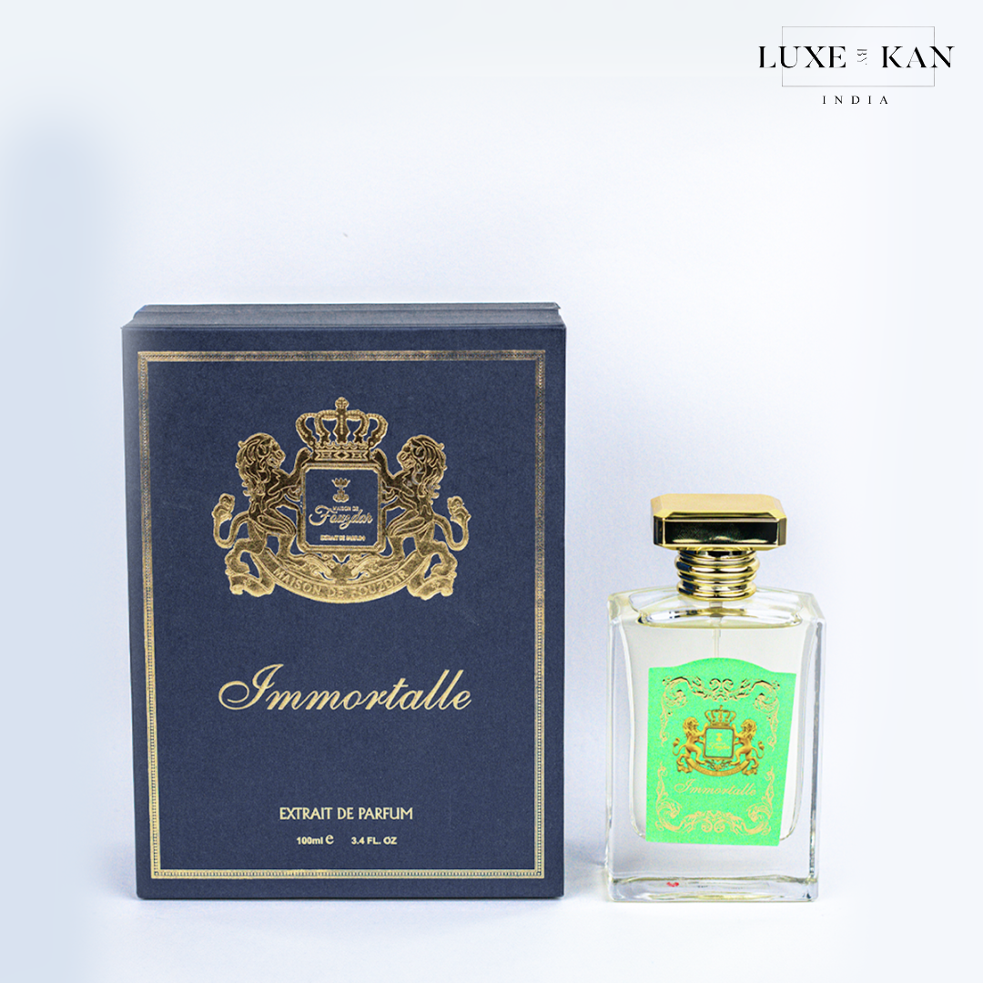 Maison de fouzdar immortalle perfume bottle next to a luxurious blue box, adorned with a golden crown and satin ribbon.