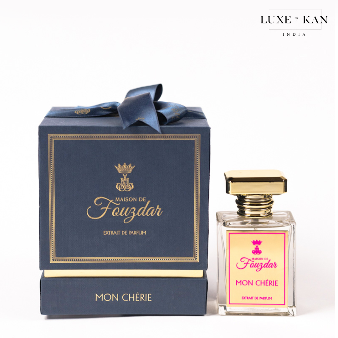 Maison de fouzdar mon cherie perfume bottle next to a luxurious blue box, adorned with a golden crown and satin ribbon.