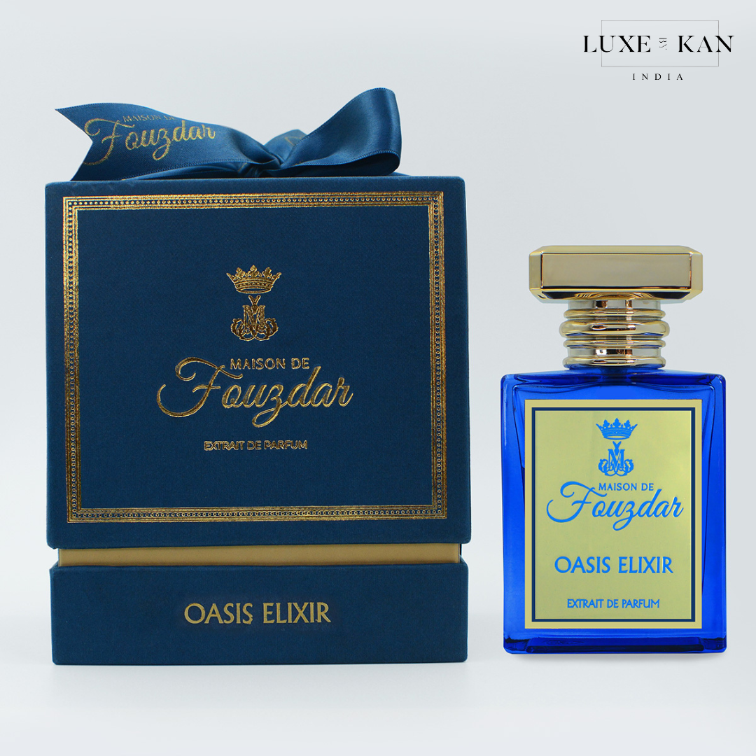 Maison de fouzdar oasis elixir perfume bottle next to a luxurious blue box, adorned with a golden crown and satin ribbon.
