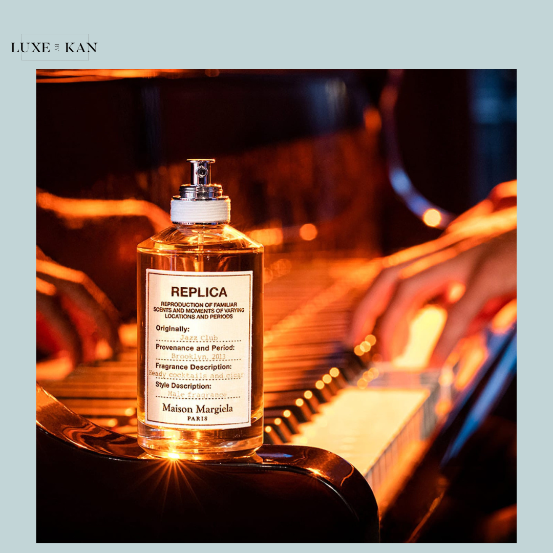 A bottle of Maison Margiela's Replica fragrance sits on a piano, illuminated by warm light, capturing a nostalgic jazz club essence.