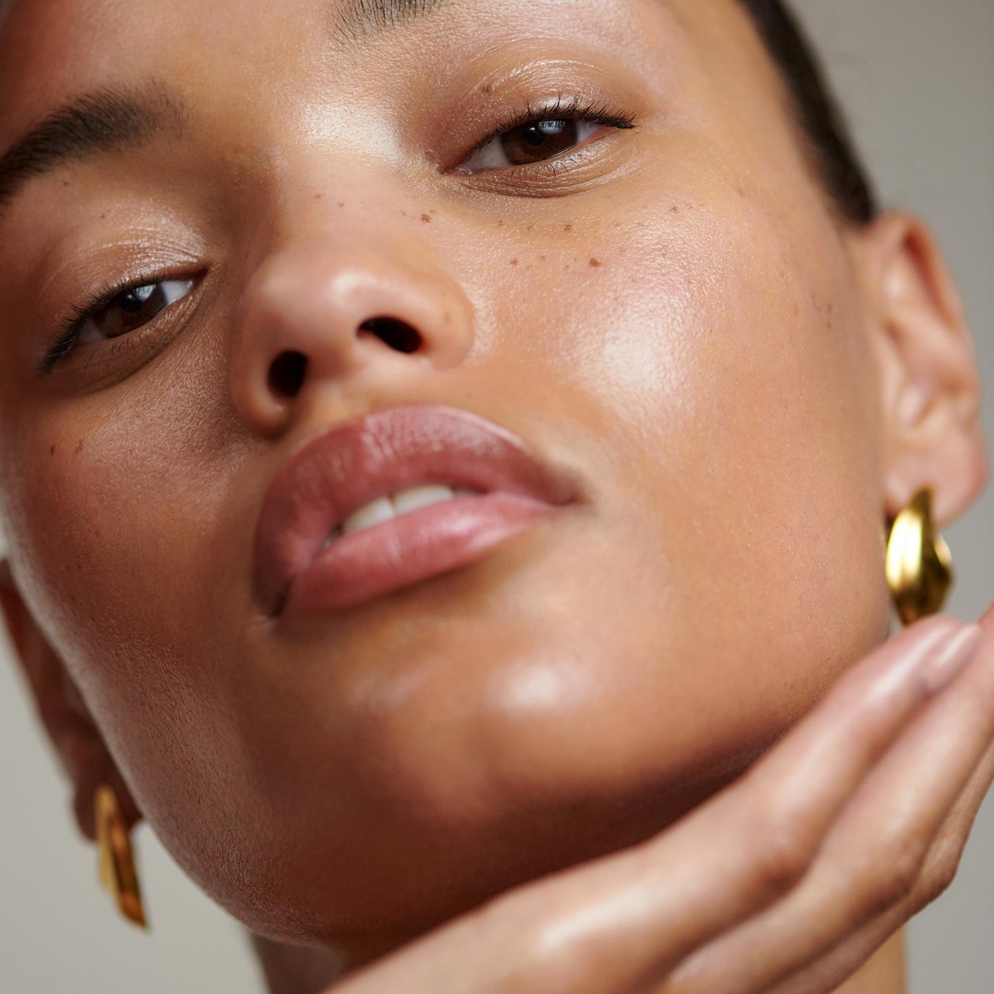 A close-up of a hand gently touching a person's face, showcasing gold hoop earrings and smooth skin tones.