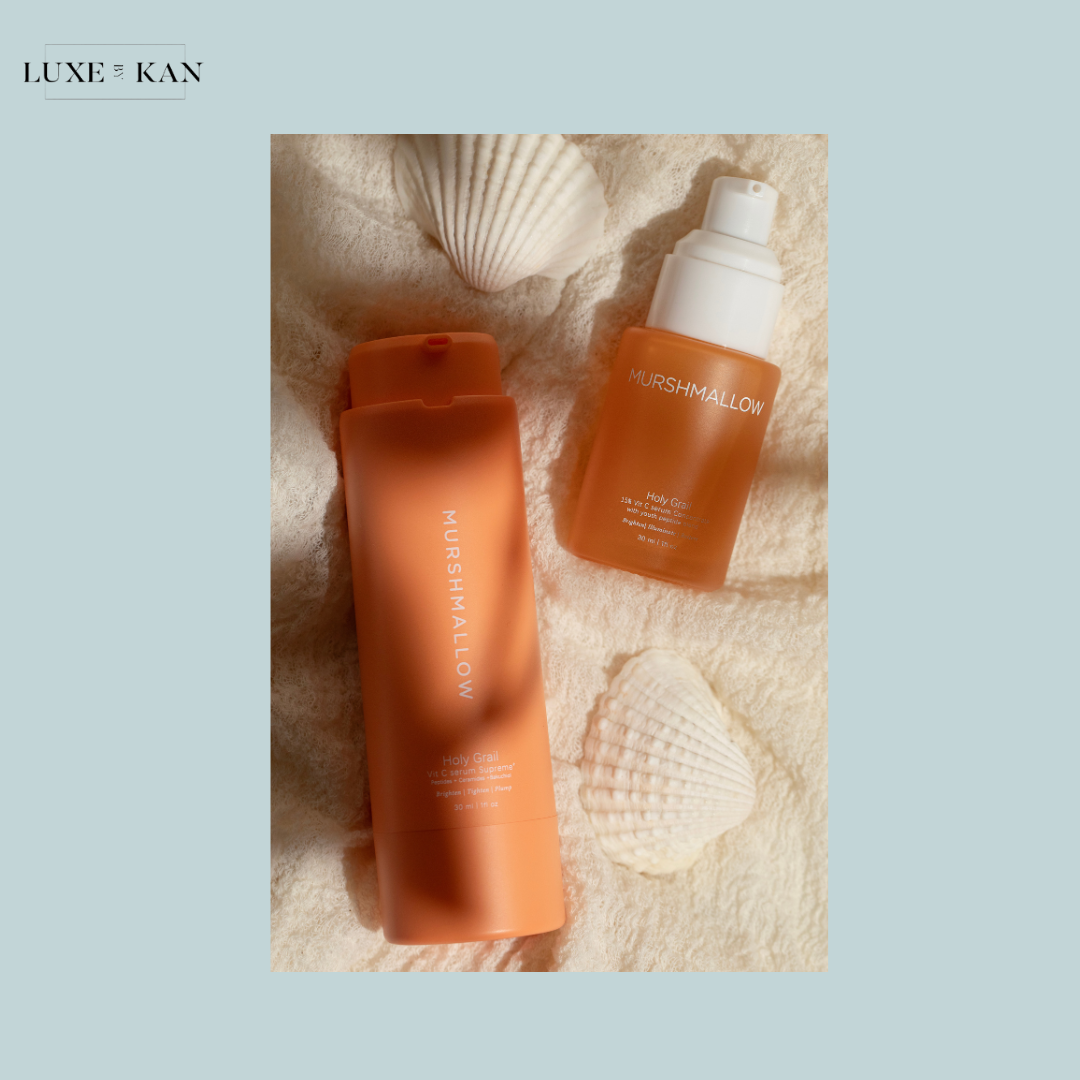 Two Murshmallow skincare products, a bottle and a pump, on a soft fabric background with seashells, exuding a coastal vibe.