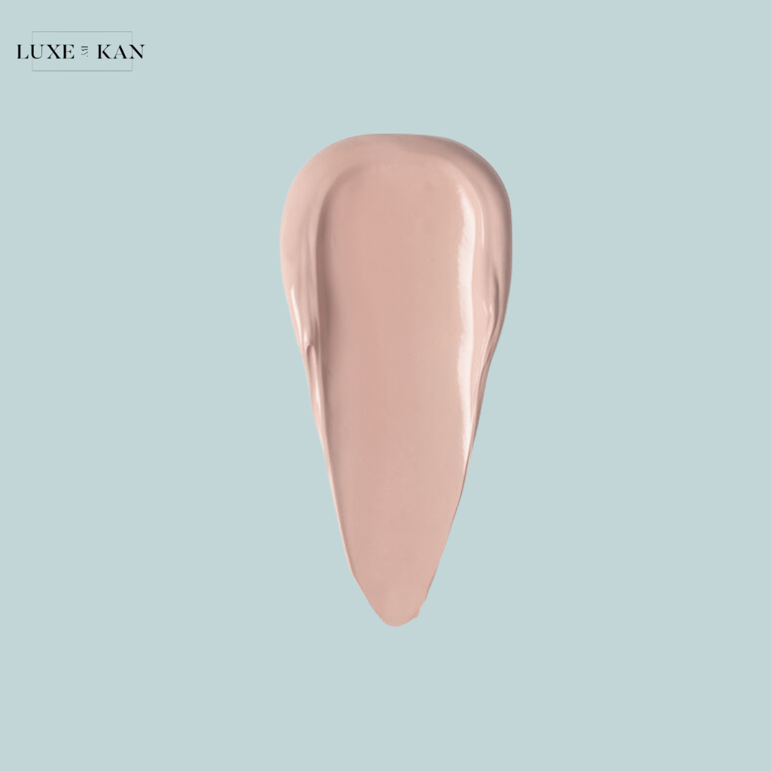 A smooth, creamy swatch of light peach-colored makeup product against a soft blue background, showcasing its texture and hues.