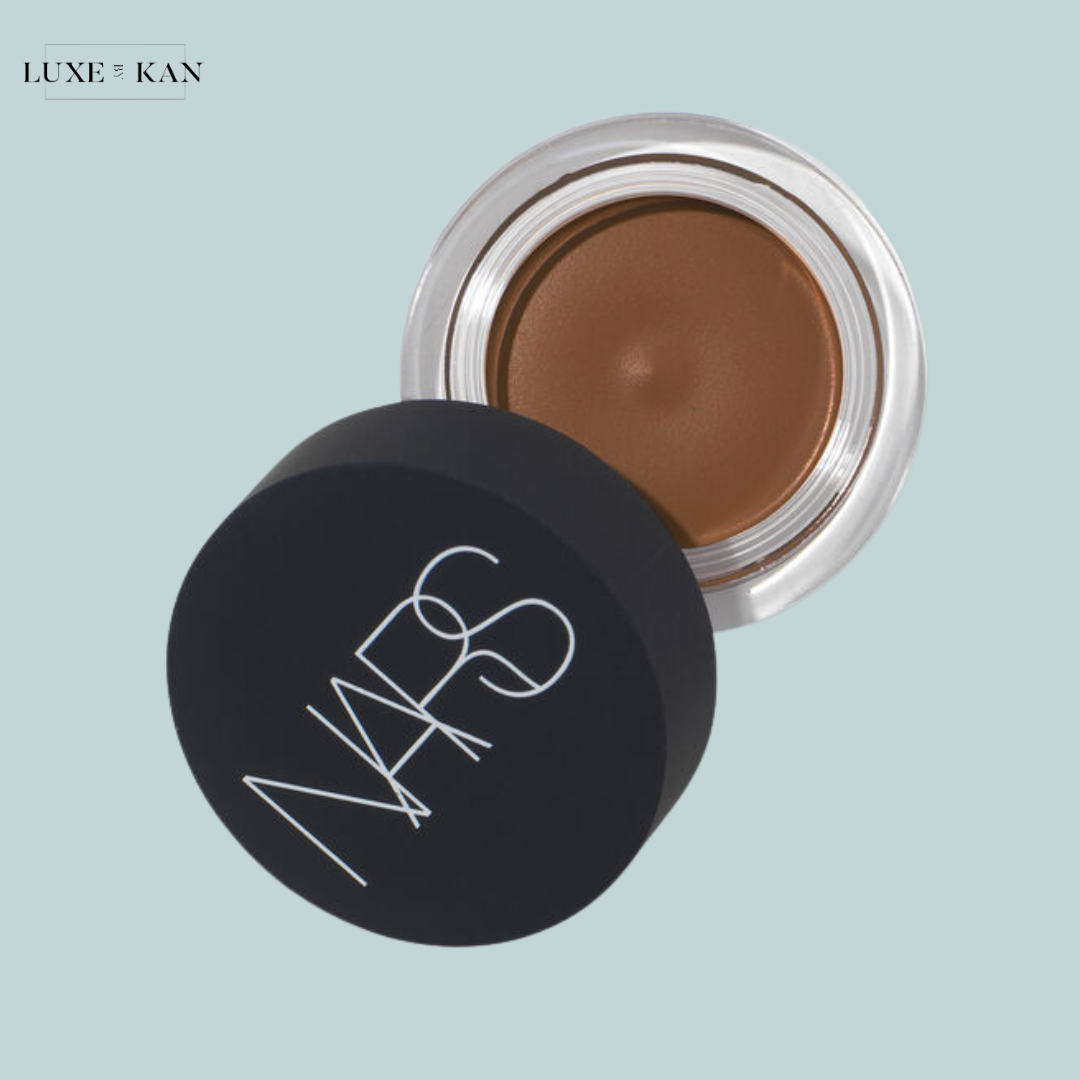 Open jar of NARS cream product on a light blue background, showcasing a rich brown shade with sleek black lid featuring the NARS logo.