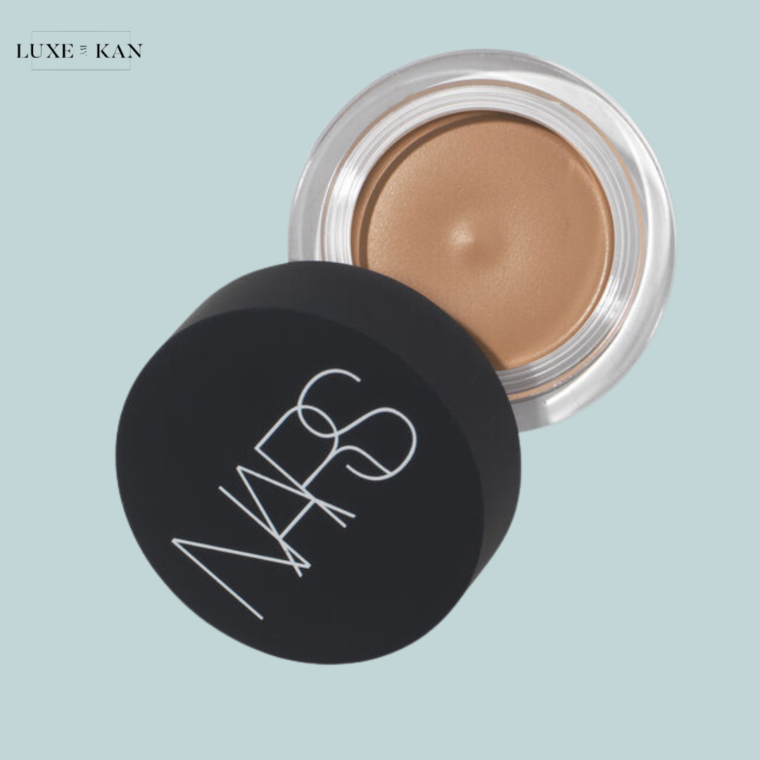 Close-up of a NARS cream product in a black container, partially open, revealing a warm beige shade.