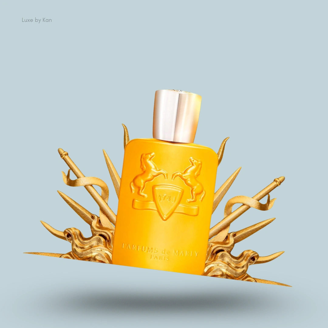 A yellow Parfums de Marly Perseus Eau de Parfum spray bottle resting on and surrounded by gold decorative spears, ribbon, and flourishes.