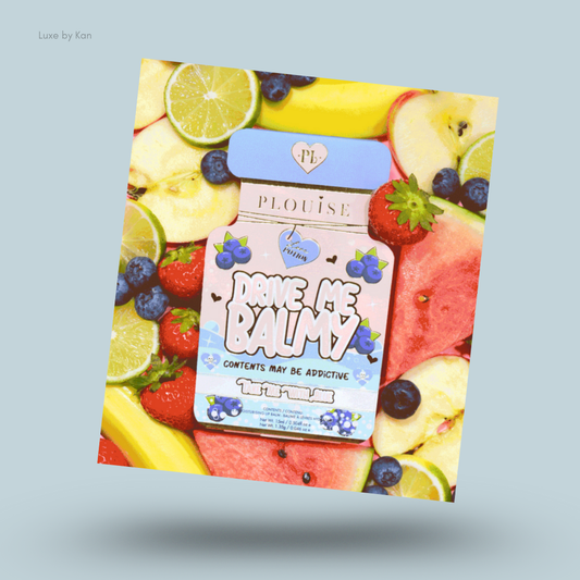 Plouise "Drive Me Balmy" lip balm duo packaging set against a backdrop of fresh fruits, including sliced apples, bananas, limes, strawberries, blueberries, and watermelon.